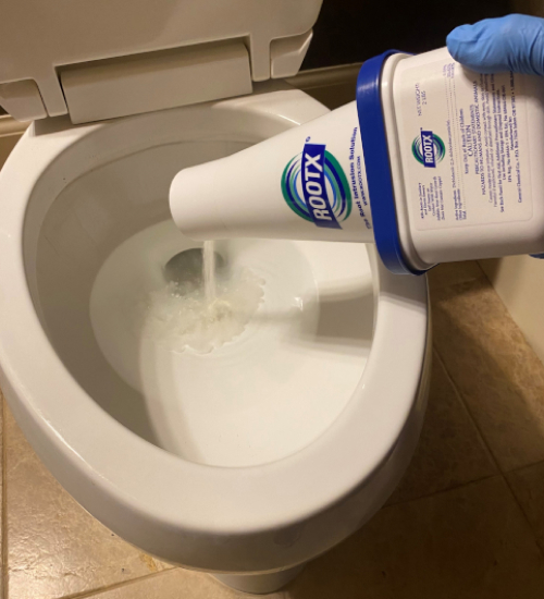 A person wearing a blue glove pours RootX into a toilet seat